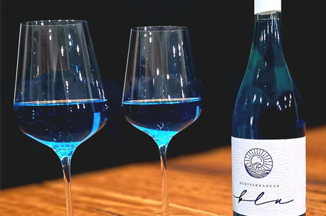 Two wine glasses filled with blue liquid next to a bottle of blue wine on a wooden surface.