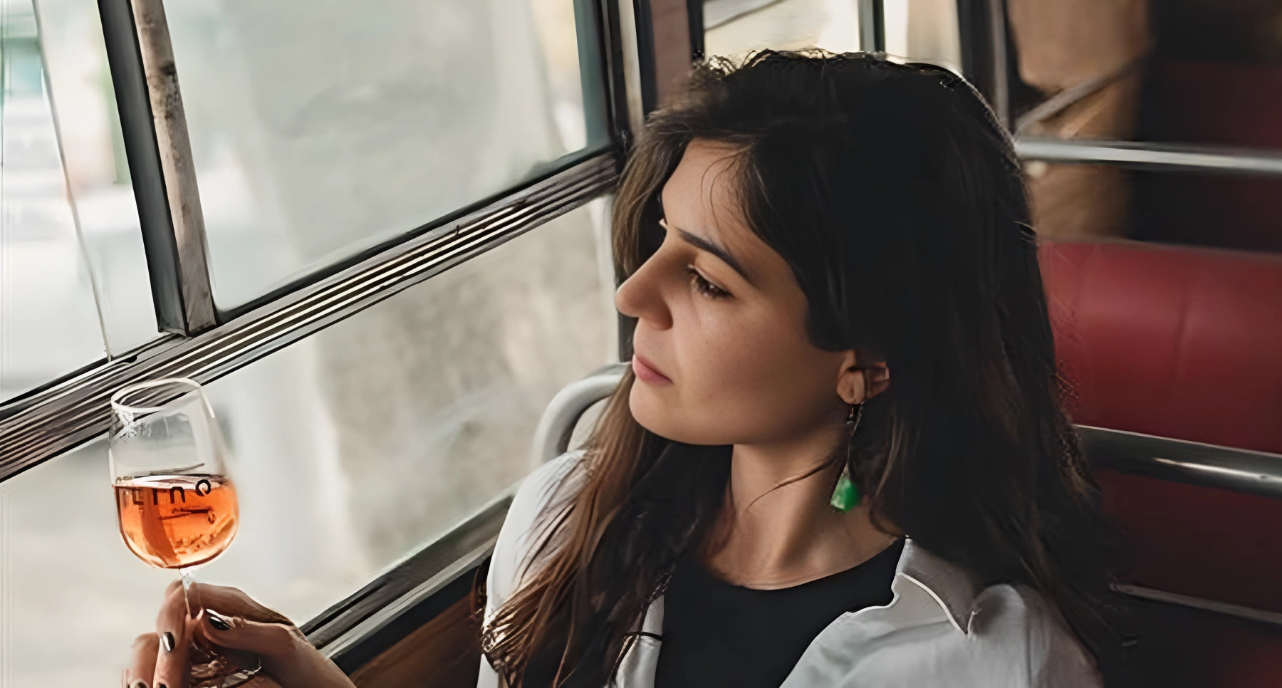 Woman sitting on a bus holding a glass of orange juice, looking out the window.
