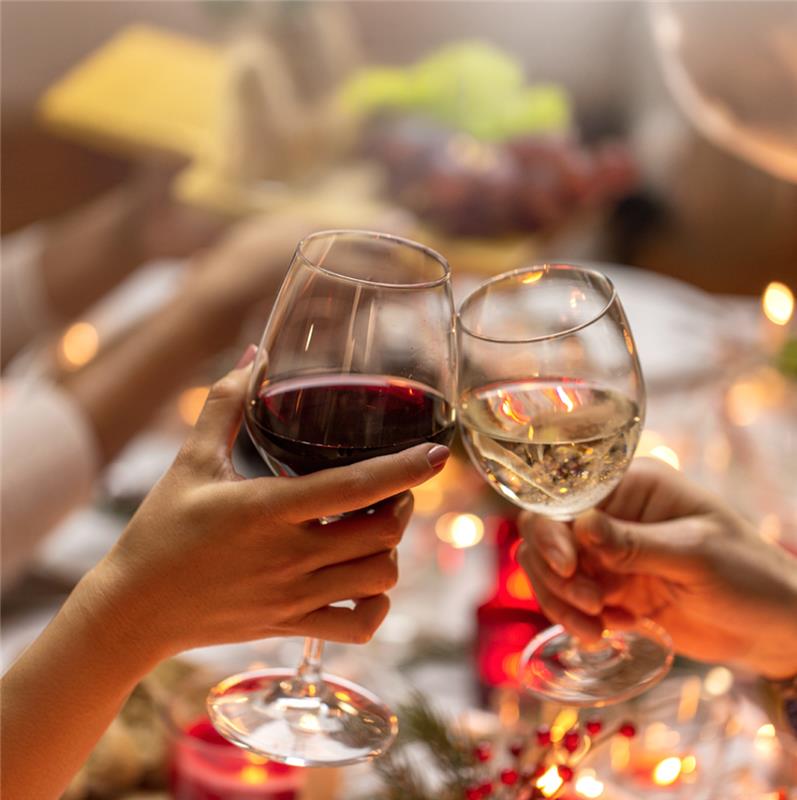 Two people clinking wine glasses with red and white wine in a festive setting.